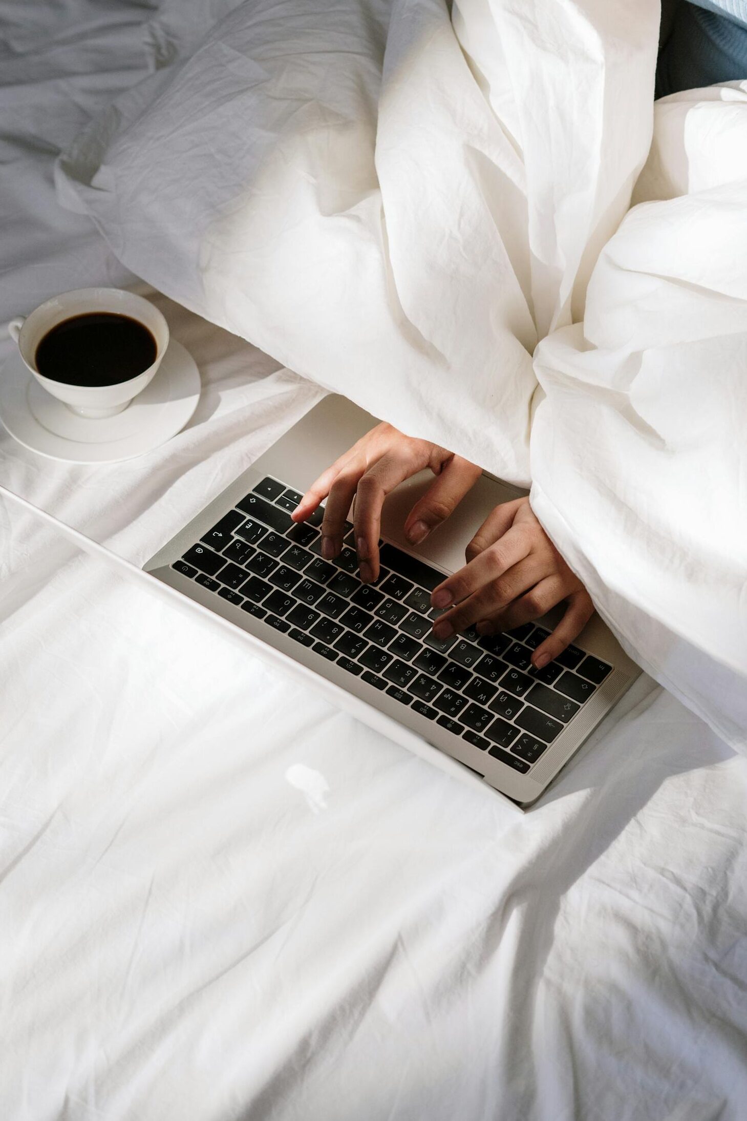 Comfortable home office setup with a laptop on bed and a cup of coffee, perfect for remote work.