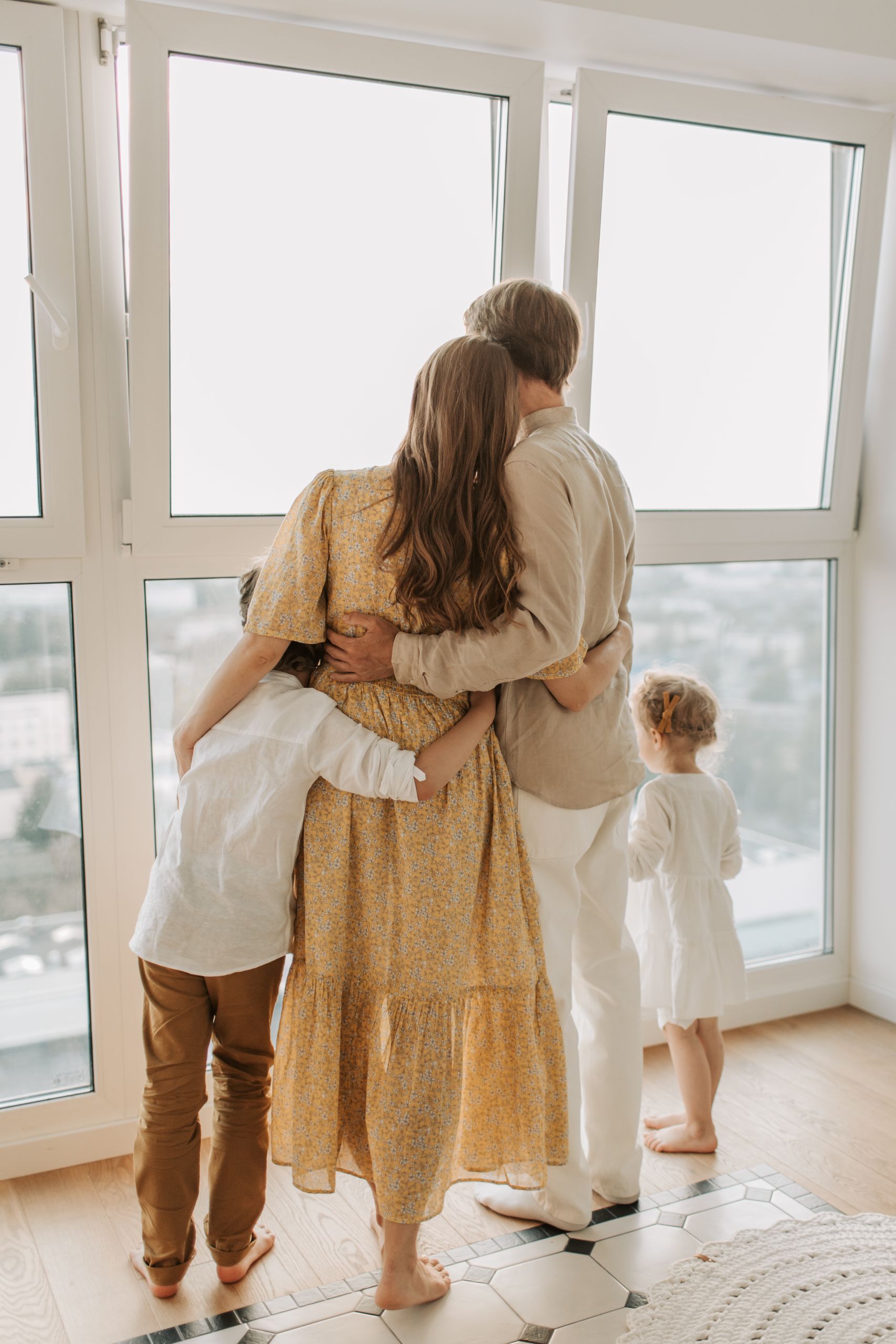 A loving family of four enjoys the view from a sunlit room, united in a warm embrace.